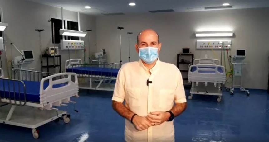 prefeito de máscara cirúrgica em pé posando para foto com leitos de hospital ao fundo